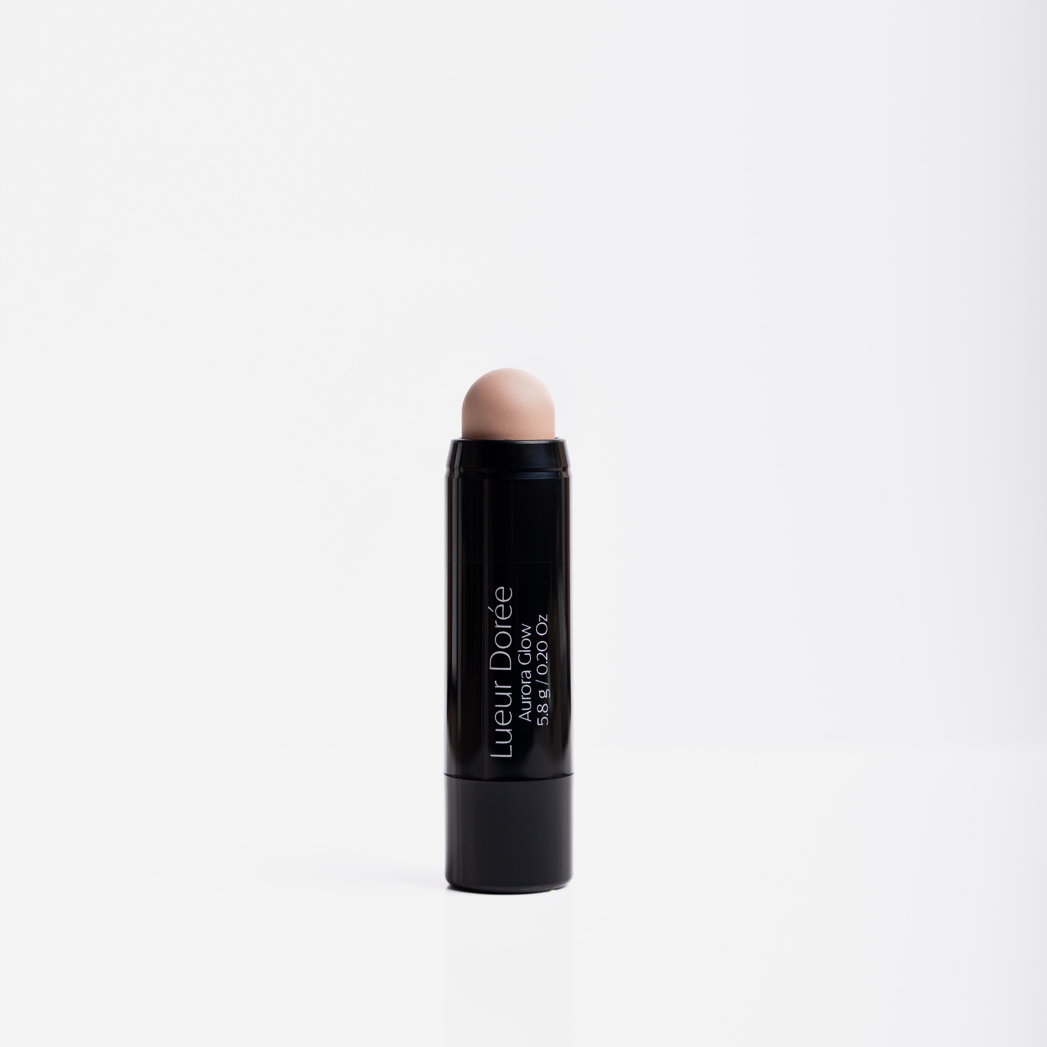 Lueur Dorée Aurora Glow highlighter stick standing upright, showcasing sleek black design and creamy highlighter tip.