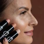 Model applying Golden Mirage - Coral Glow Highlighter No.3 on cheekbones, showcasing luminous finish and multi-stick versatility.
