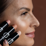 Model applying Golden Mirage - Coral Glow Highlighter No.3 on cheekbones, showcasing luminous finish and multi-stick versatility.