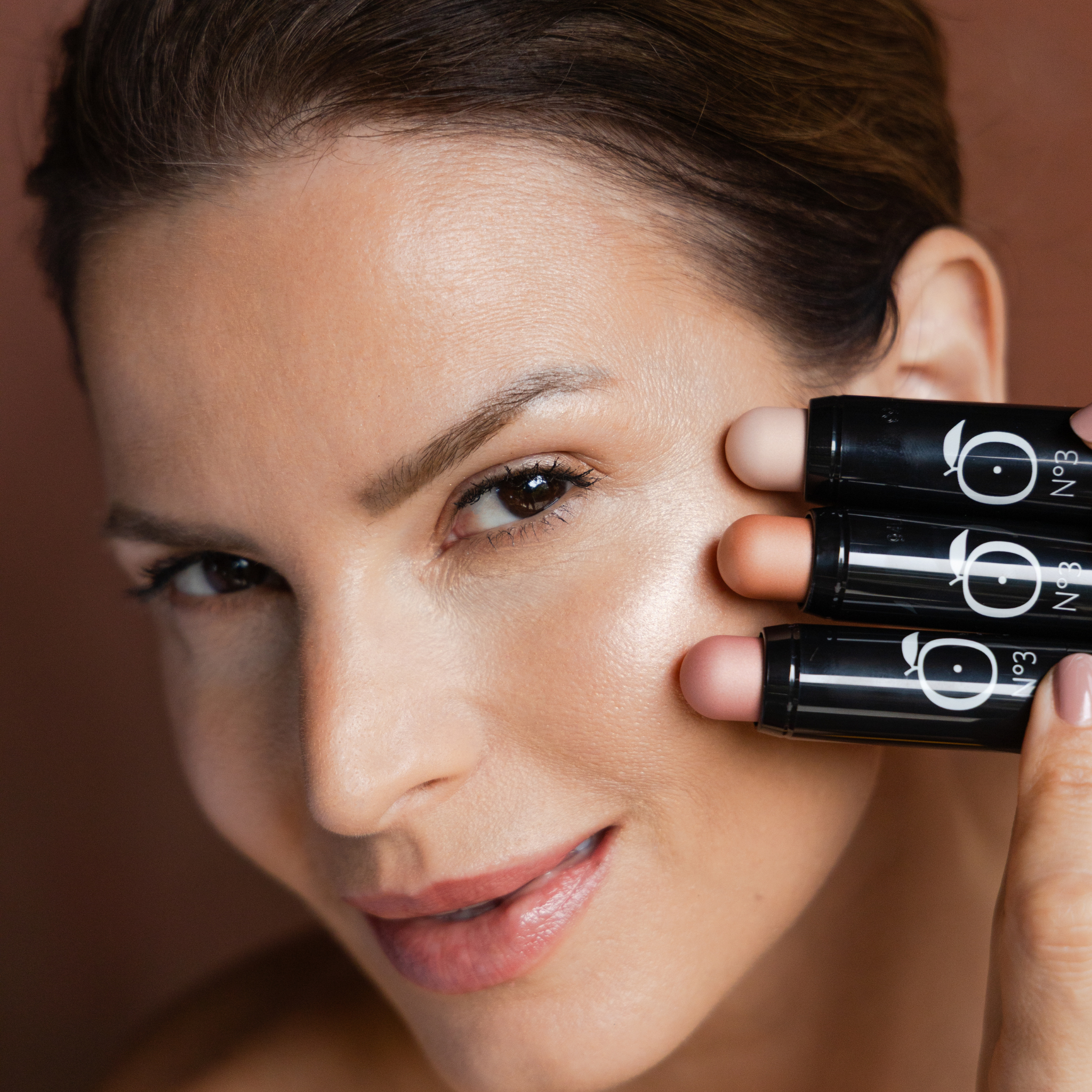Model applying Lueur Dorée Highlighter Sticks in three shades for a dewy glow and luminous finish on mature skin.