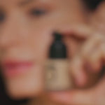 Blurred image of person holding Teint Naturelle Foundation. Focus on product's compact, elegant design.
